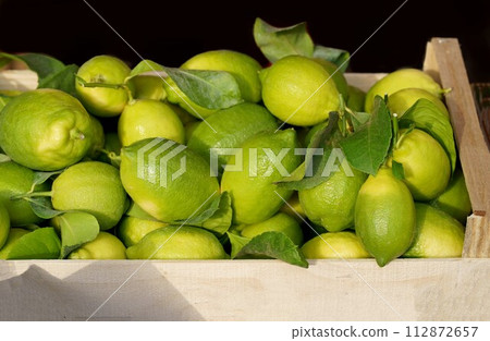 Lemons in a box at the market. Fresh lemon with leaves. Lemon Tree. Box of yellow lemons with fresh lemon tree leaves 112872657