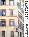 Windows of Rome. Classic old wooden windows with blue shutters in a public place on a city street or in an urban environment. Image of the Mother of God on the facade of the house 112872672