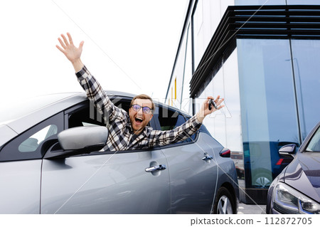 Excited young man showing a car key, sitting inside his new vehicle 112872705