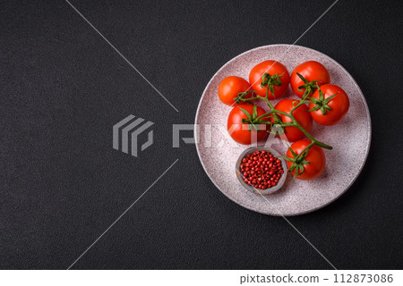 Fresh red cherry tomatoes on a branch on a dark concrete background Fresh red cherry tomatoes on a branch on a dark concrete background 112873086