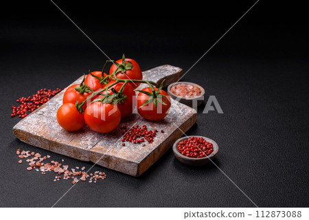 Fresh red cherry tomatoes on a branch on a dark concrete background Fresh red cherry tomatoes on a branch on a dark concrete background 112873088