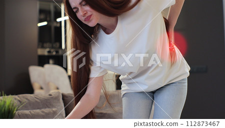 Girl suffers from backache feeling badly, sitting on couch in living room at home. 3d animation with red pulsating sore zone of problem area. People health care problem. 112873467
