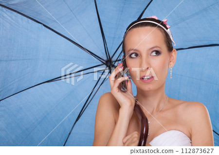 Bride woman with umbrella talking on mobile phone. 112873627