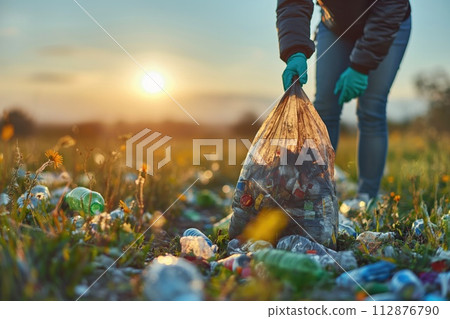 AI-generated content. Volunteer in gloves stands holding a bag of litter in a field, illuminated by the soft light of dawn. 112876790
