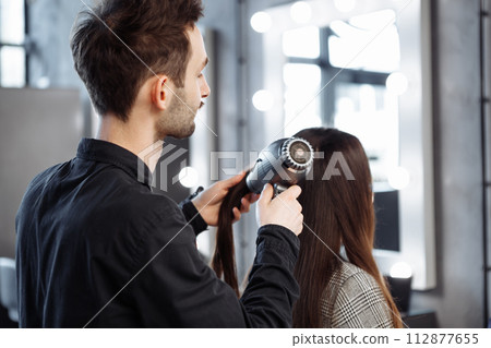 The master does hair styling in a beauty salon. Young woman preparing for a date. The master does hair styling in a beauty salon. Young woman preparing for a date. 112877655