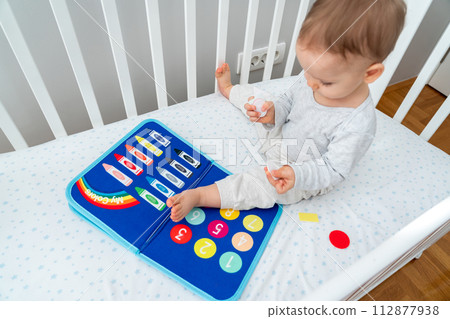 Baby playing with busy book sitting in crib. Concept of smart books and modern toys 112877938