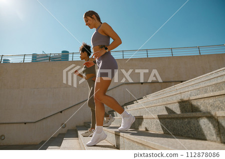 Side view of athletic women in sportswear are jogging around the city in morning. Reaching the goal Side view of athletic women in sportswear are jogging around the city in morning. Reaching the goal 112878086
