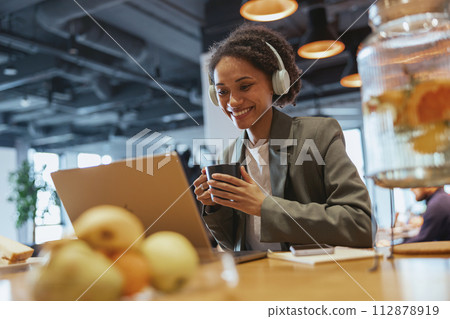 A woman with a smile is sitting at a wood table using a laptop computer 112878919