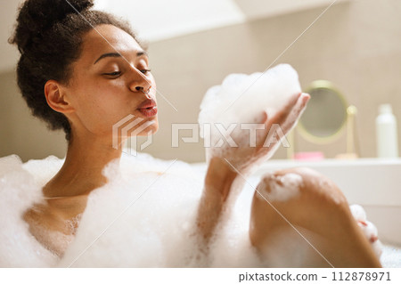 A happy woman bathing in a foamy spa tub, gesturing artfully with eyelashes 112878971