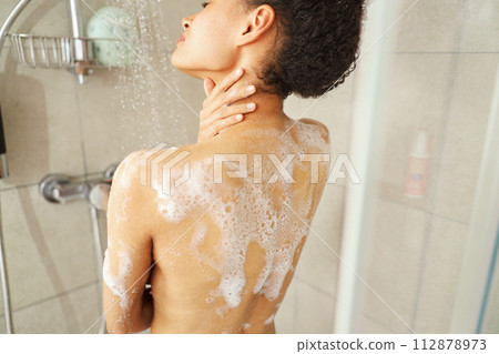 A woman is showering with soap on her back, washing her chest and waist 112878973