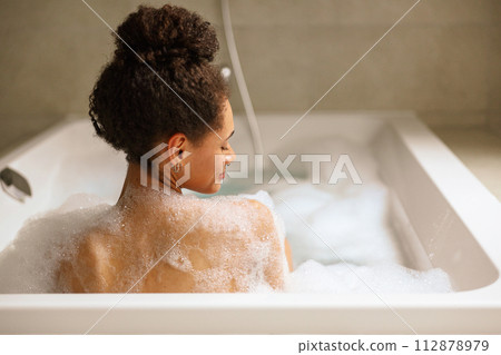A woman is bathing in a foamy bathtub in the bathroom 112878979
