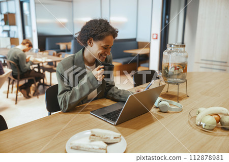 A woman sits at a desk with a laptop and coffee on a wooden table 112878981
