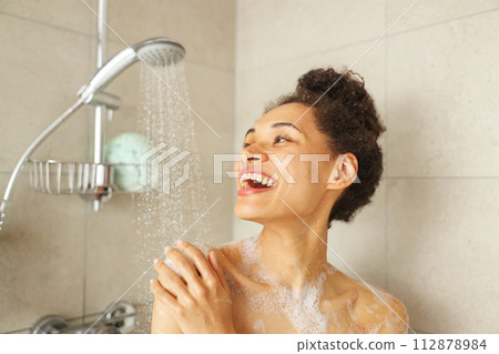 A woman in the shower, smiling and enjoying the water from the plumbing fixture 112878984