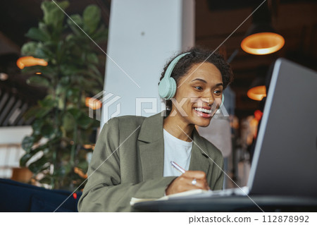 A woman in a suit is smiling in front of a laptop computer with headphones 112878992