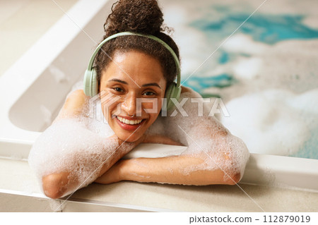 a woman wearing headphones is taking a bath in a hot tub 112879019