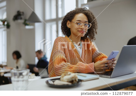 A freelancer worker is seated at a desk with a laptop and cell phone in a modern cafe 112879077