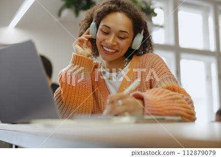 a woman wearing headphones is sitting at a table with a laptop and a pen 112879079