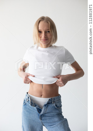 Beautiful blonde girl in a white T-shirt and blue jeans and sneakers posing on a white background Beautiful blonde girl in a white T-shirt and blue jeans and sneakers posing on a white background 112881971
