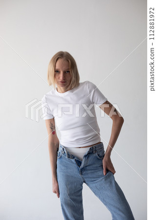 Beautiful blonde girl in a white T-shirt and blue jeans and sneakers posing on a white background Beautiful blonde girl in a white T-shirt and blue jeans and sneakers posing on a white background 112881972