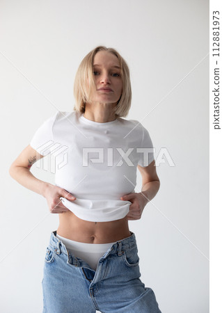 Beautiful blonde girl in a white T-shirt and blue jeans and sneakers posing on a white background 112881973