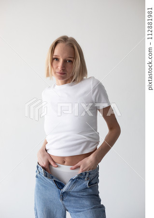 Beautiful blonde girl in a white T-shirt and blue jeans and sneakers posing on a white background Beautiful blonde girl in a white T-shirt and blue jeans and sneakers posing on a white background 112881981