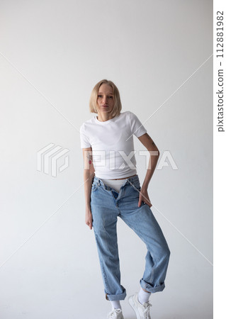 Beautiful blonde girl in a white T-shirt and blue jeans and sneakers posing on a white background Beautiful blonde girl in a white T-shirt and blue jeans and sneakers posing on a white background 112881982
