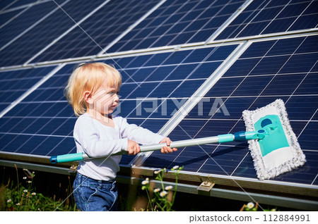 Small boy learning how to care about solar panels. Young kid cleaning new solar battery at warm sunny day. Concept of young generation and alternative energy. 112884991