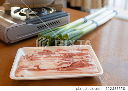 A shabu-shabu set is placed on the table, a cassette stove, white onions and pork slices A shabu-shabu set is placed on the table, a cassette stove, white onions and pork slices 112885558