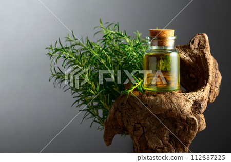 Rosemary essential oil and fresh rosemary with old snag on a stone background. Rosemary essential oil and fresh rosemary with old snag on a stone background. 112887225