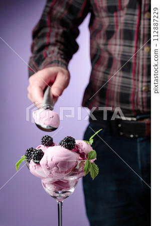 Man puts blackberry ice cream in a sundae cup. 112887229