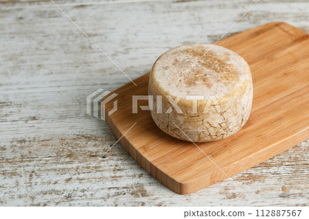 Artisanal and natural whole cheese, placed on a wooden board and without labels. 112887567