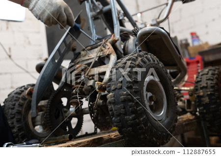 A man finishes repairing an ATV in his garage. A man repaired his son's little red four-wheeler in his garage and replaced the broken parts with new ones. Broken quad bike concept. A man finishes repairing an ATV in his garage. A man repaired his son's little red four-wheeler in his garage and replaced the broken parts with new ones. Broken quad bike concept. 112887655