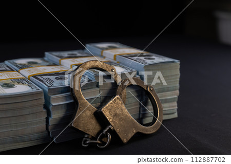 Paper dollars lie on a black background with handcuffs. Many dollars and handcuffs are neatly layered on a black background. Crime and money concept. Paper dollars lie on a black background with handcuffs. Many dollars and handcuffs are neatly layered on a black background. Crime and money concept. 112887702