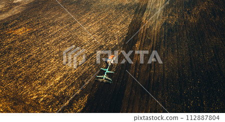Aerial View. Tractor Plowing Field In Spring Season. Beginning Of Agricultural Spring Season. Cultivator Pulled By A Tractor In Countryside Rural Field Landscape Aerial View. Tractor Plowing Field In Spring Season. Beginning Of Agricultural Spring Season. Cultivator Pulled By A Tractor In Countryside Rural Field Landscape 112887804