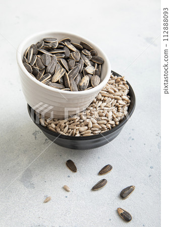 Bowls with peeled and whole raw and salted sunflower seeds on light table. 112888093