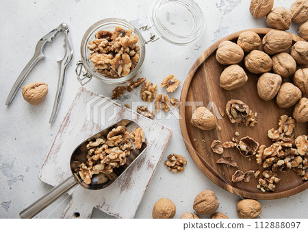 Wooden plate with whole and peeled walnut nuts with scoop and cracker on light background. Wooden plate with whole and peeled walnut nuts with scoop and cracker on light background. 112888097
