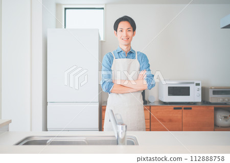 一個穿著圍裙的男人站在廚房裡 一個穿著圍裙的男人站在廚房裡 112888758