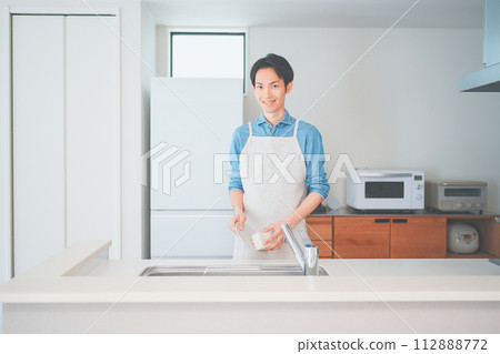 一個穿著圍裙的男人在廚房洗碗 一個穿著圍裙的男人在廚房洗碗 112888772