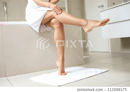 A woman is seated on a bathtub, with her legs crossed 112889175