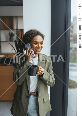 a woman is talking on a cell phone while holding a cup of coffee a woman is talking on a cell phone while holding a cup of coffee 112889212