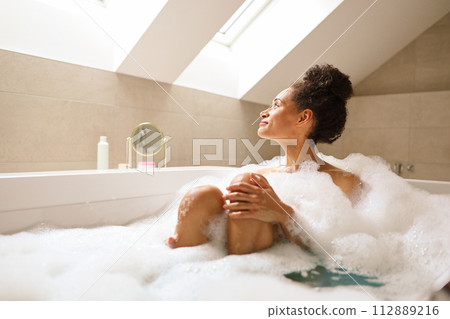 Woman relaxing in bathtub full of foam in bathroom of house Woman relaxing in bathtub full of foam in bathroom of house 112889216