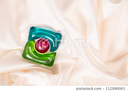 Liquid detergent gel in capsule on fabric close-up, space for text 112890063