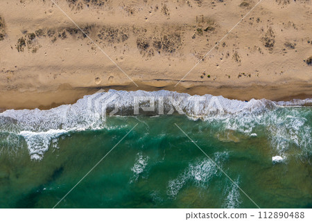 Aerial view of ocean waves washing a sandy shoreline 112890488