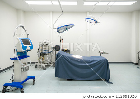 A typical operating room in a hospital with surgical light overhead for providing bright, directional lighting to the surgical team during procedure. The operating table is at the center of the room. A typical operating room in a hospital with surgical light overhead for providing bright, directional lighting to the surgical team during procedure. The operating table is at the center of the room. 112891320