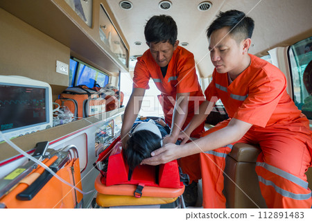 Two paramedics in orange uniforms are helping a patient inside an ambulance. Two paramedics in orange uniforms are helping a patient inside an ambulance. 112891483