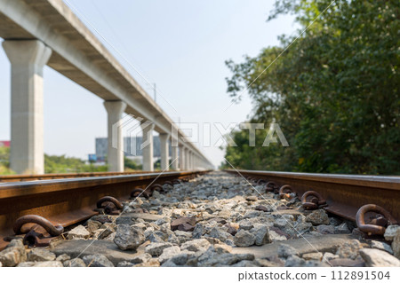 Closeup of railway track, a shallow depth of field focusing on the railroad ties and rocks on the track. Metal rails are fastened to the ties with clips or spikes, which help keep the rails in place. 112891504