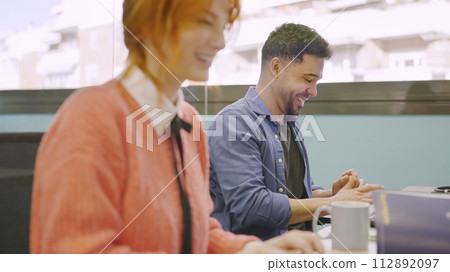 Coworkers smiling while working together with computers Coworkers smiling while working together with computers 112892097