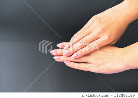 A beautiful woman's hand on a dark background. The hands are thin, the fingers are natural, and the skin is dry. Light pink fingertips. 112892189