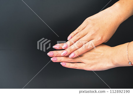 A beautiful woman's hand on a dark background. The hands are thin, the fingers are natural, and the skin is dry. Light pink fingertips. 112892190