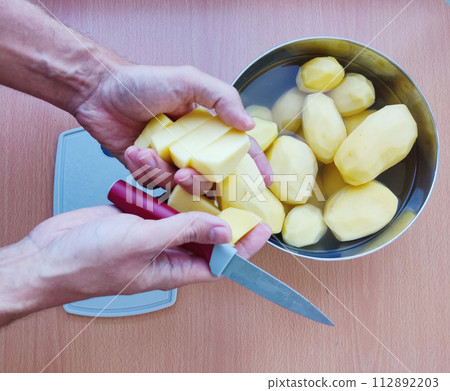 Close up of man holding and peeling potato. Hands cutting potatoes at kitchen to prepare a recipe. 112892203